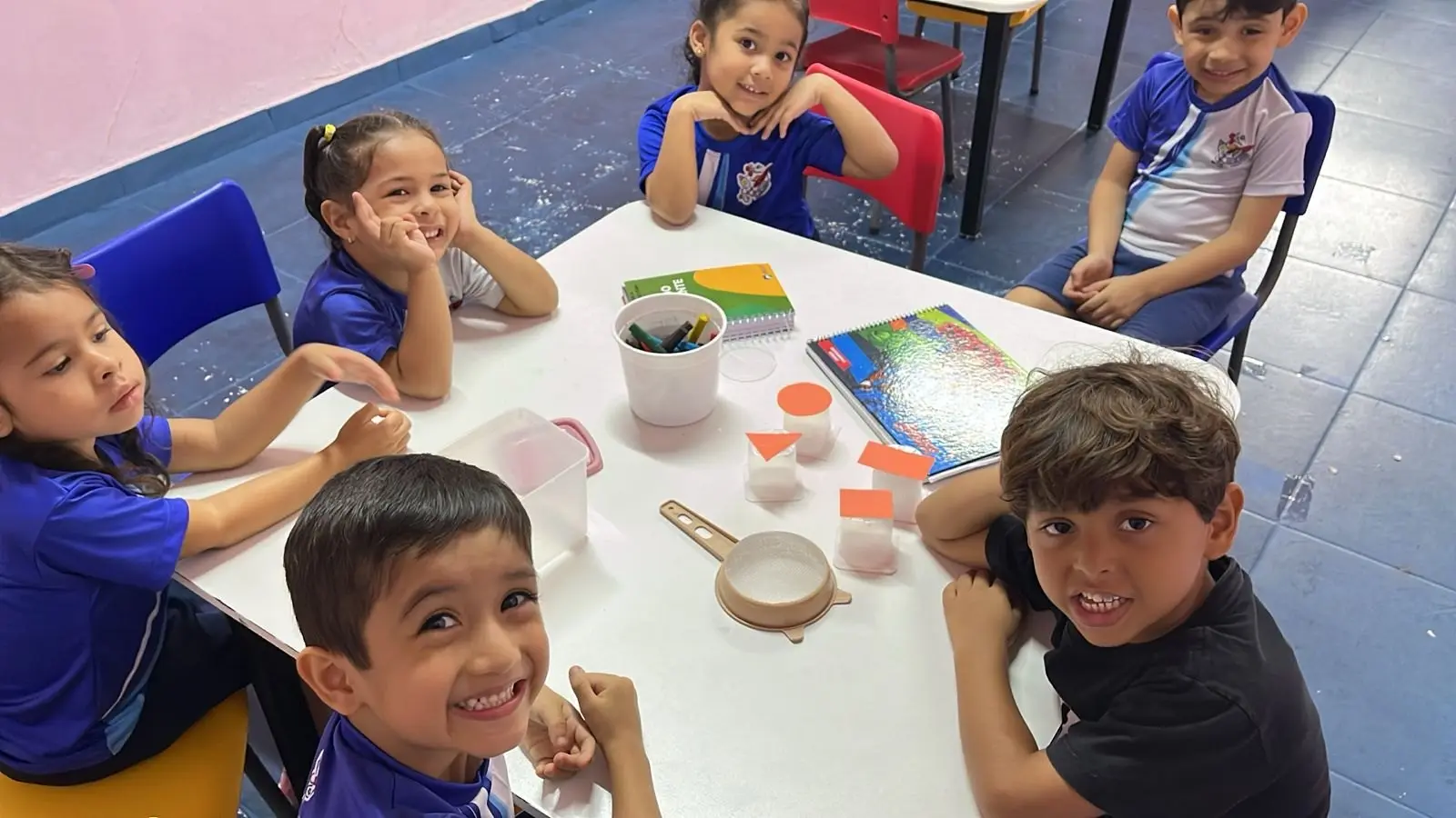 Crianças sorrindo à mesa durante uma atividade com tinta e massinha