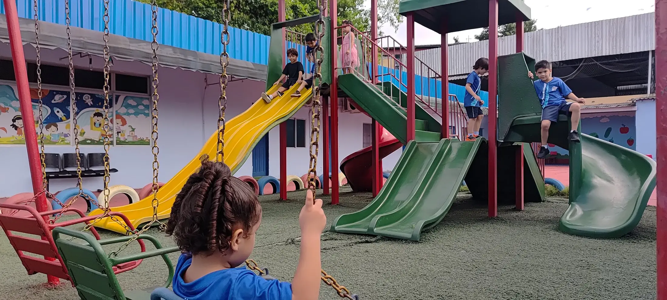 Criança no balanço, com o parquinho ao fundo