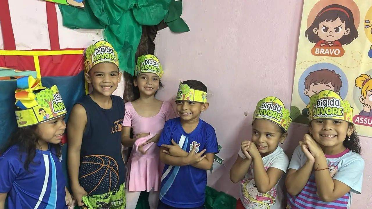 Crianças sorrindo com faixas de papel verde escritas Dia da Árvore na testa