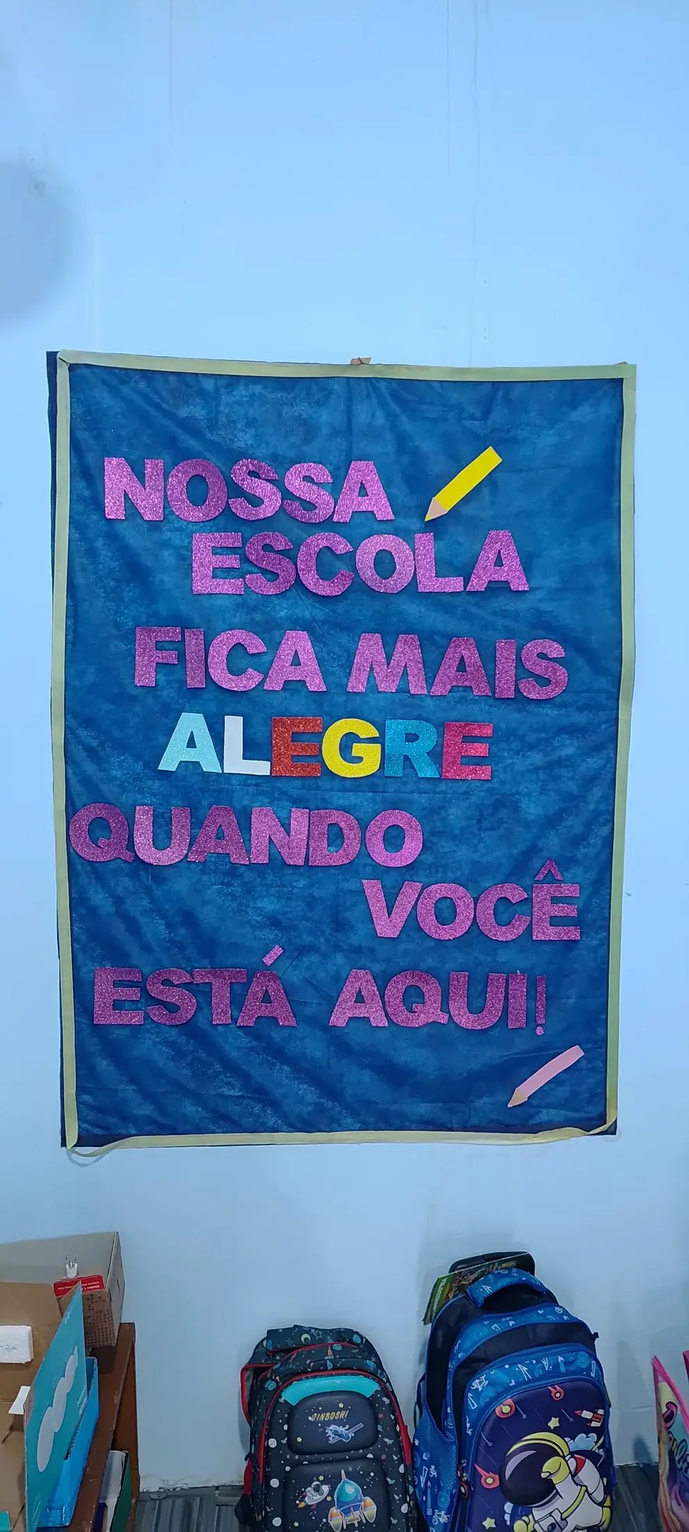 Painel na parede da escola com a frase: Nossa escola fica mais alegre quando você está aqui