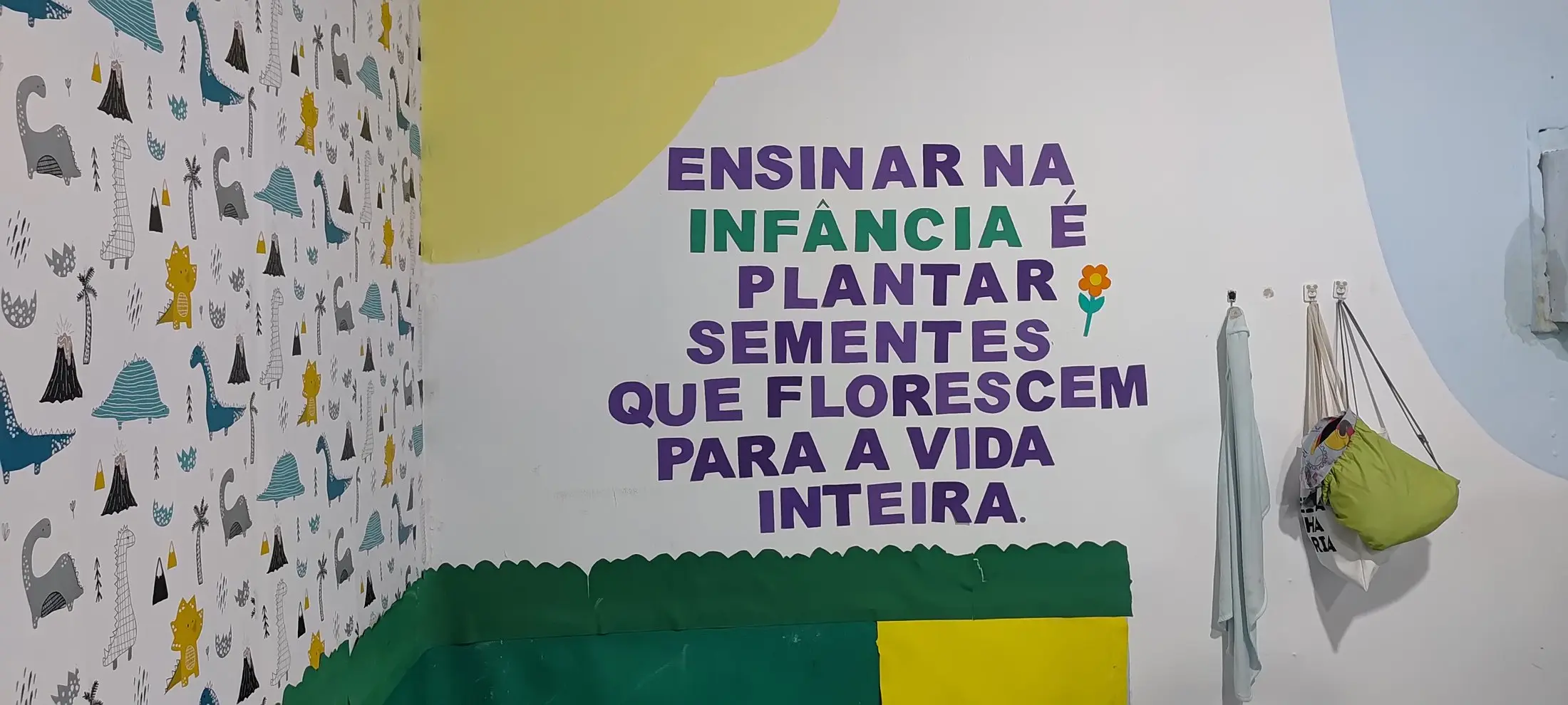 Frase pintada na parede: Ensinar na infância é plantar sementes que florescem para a vida inteira