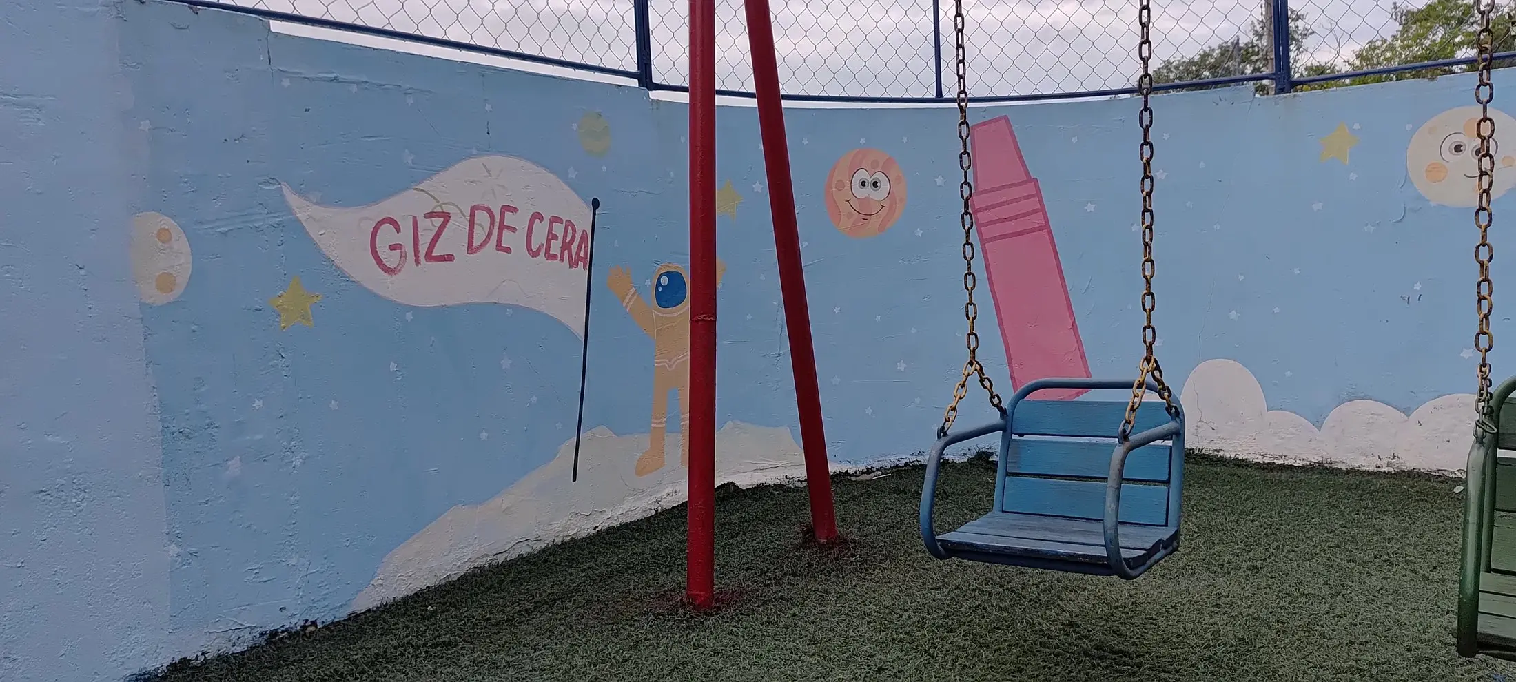 Muro do pátio pintado com o nome Giz de Cera, ao lado de um balanço