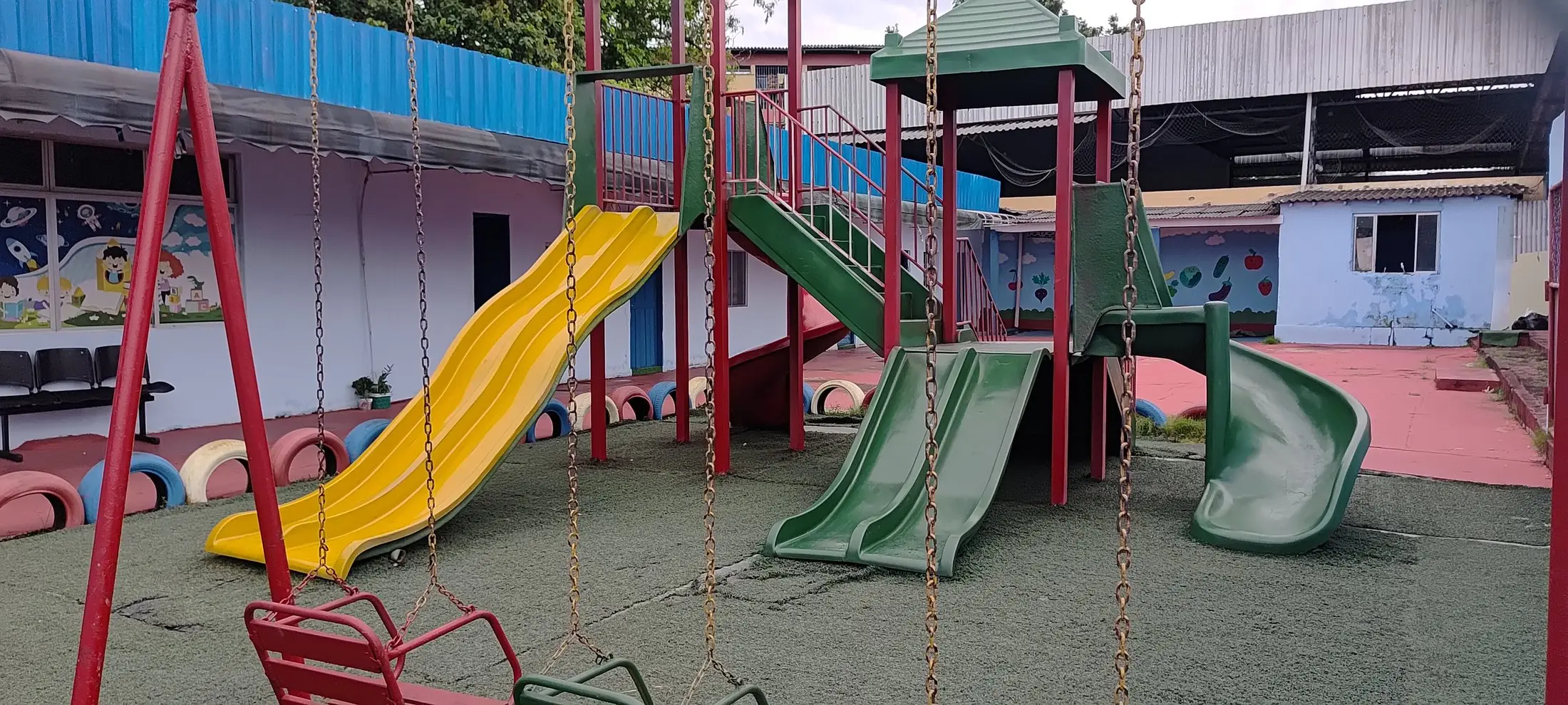 Parquinho com escorregadores amarelo e verdes, balanços coloridos e pneus pintados