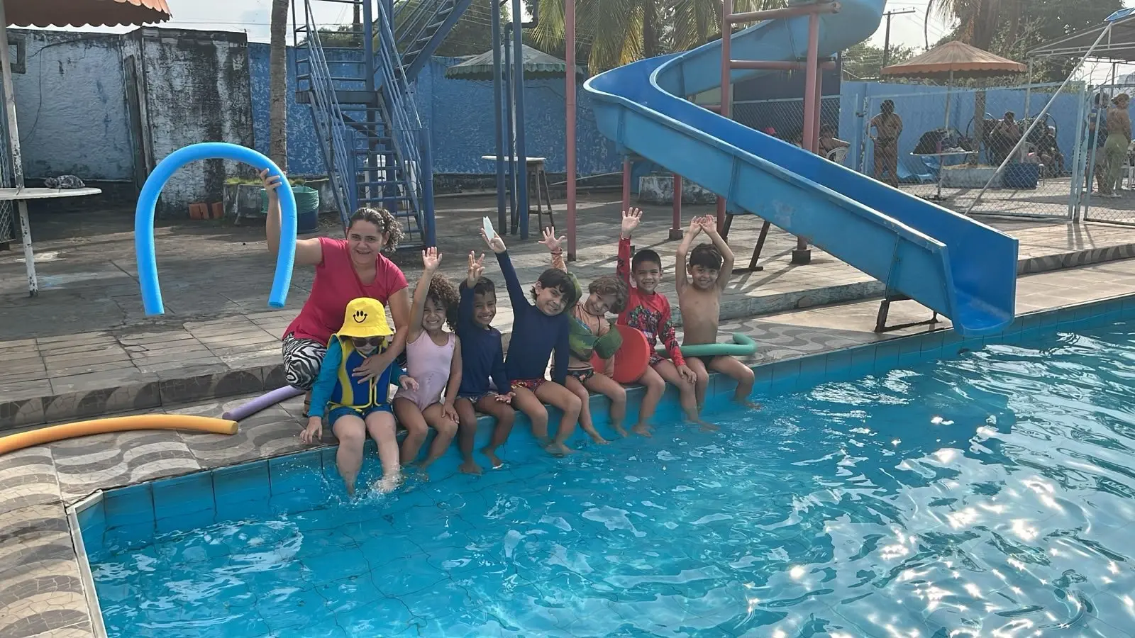 Professora e crianças de colete sentadas na borda da piscina
