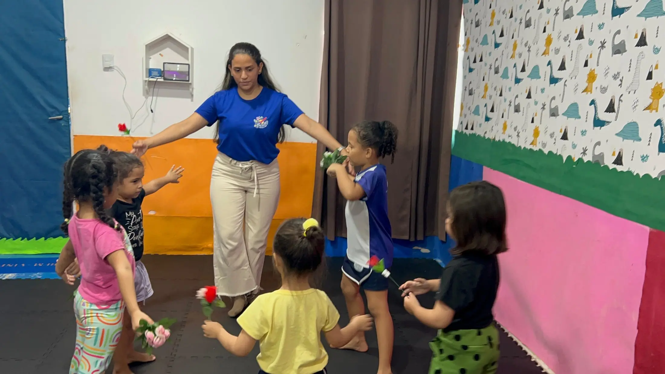 Crianças pequenas em roda com a professora, segurando flores de papel