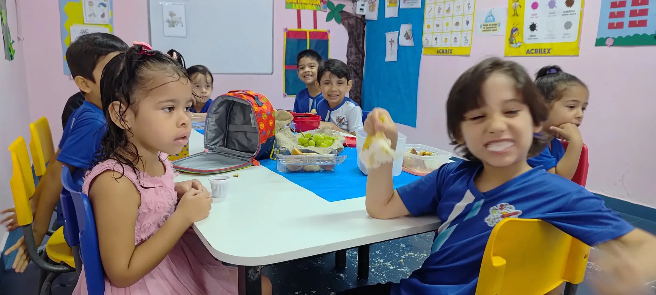 Crianças sorrindo à mesa na hora do lanche, em sala